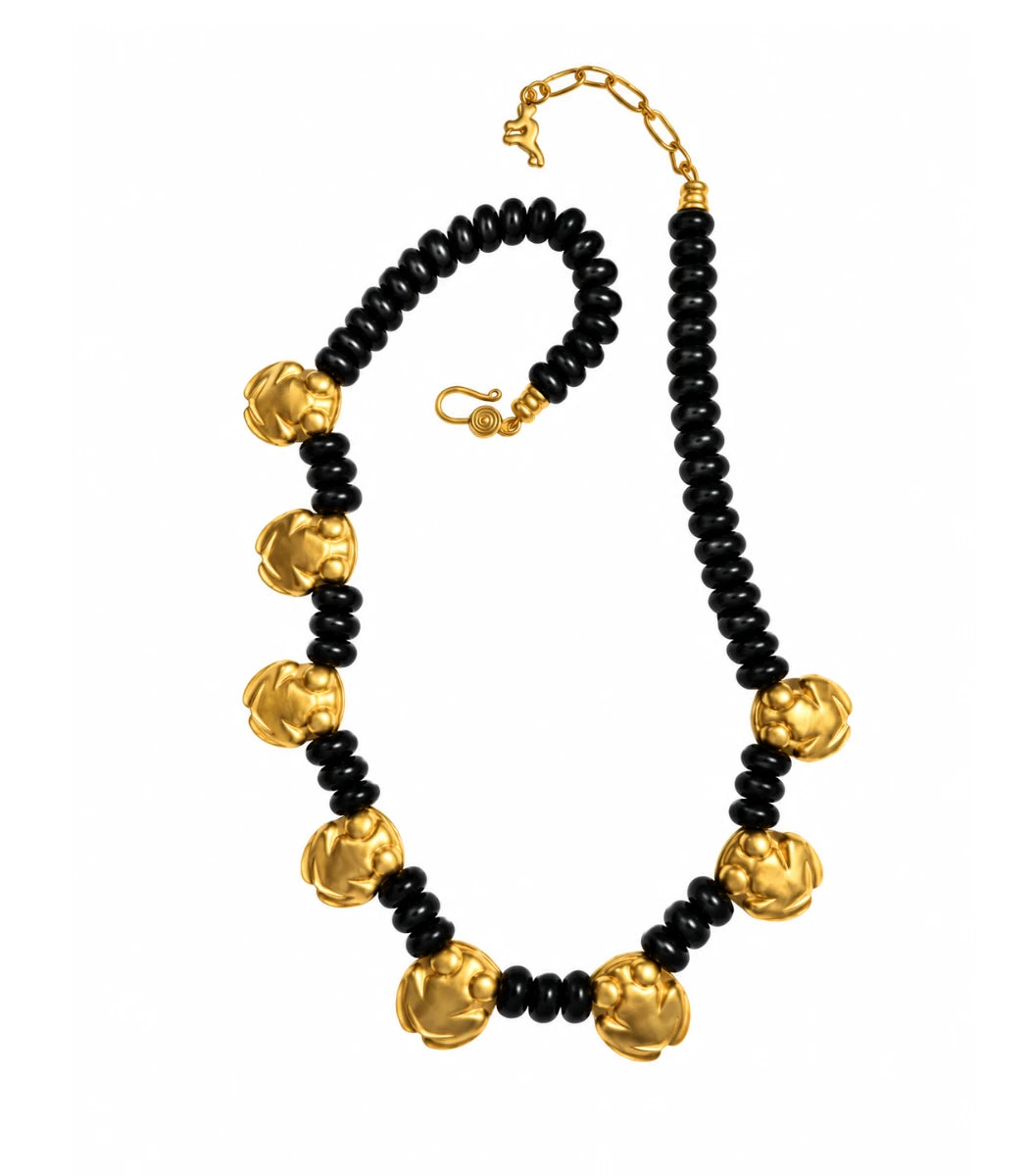 A black beaded necklace with alternating large textured gold flower-shaped beads and small black spacer beads, finished with gold hardware on a white background.