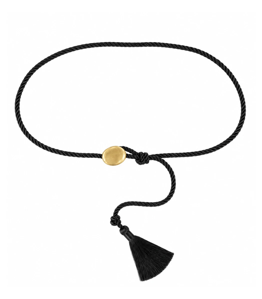 A black braided cord bracelet with a small round gold-tone bead, a knotted closure, and a black tassel, shown on a plain white background.
