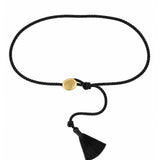 A black braided cord bracelet with a small round gold-tone bead, a knotted closure, and a black tassel, shown on a plain white background.