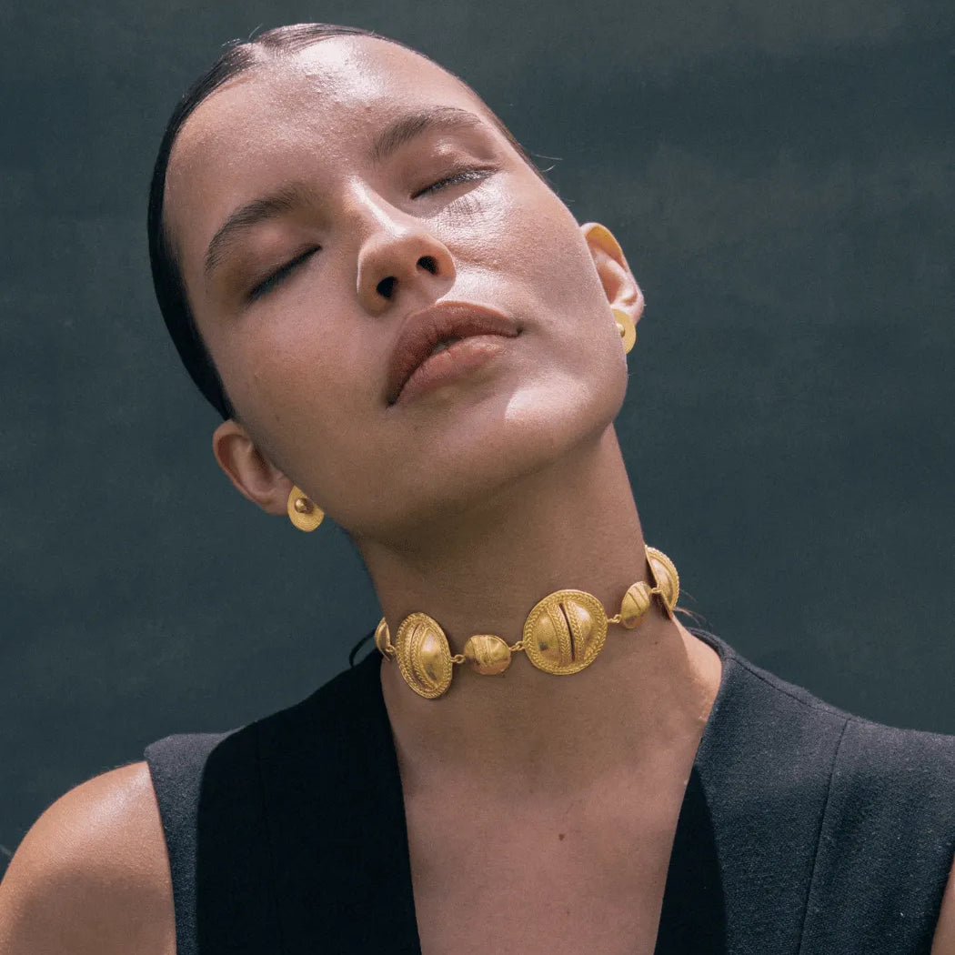 Woman wearing a gold necklace and earrings against a dark background