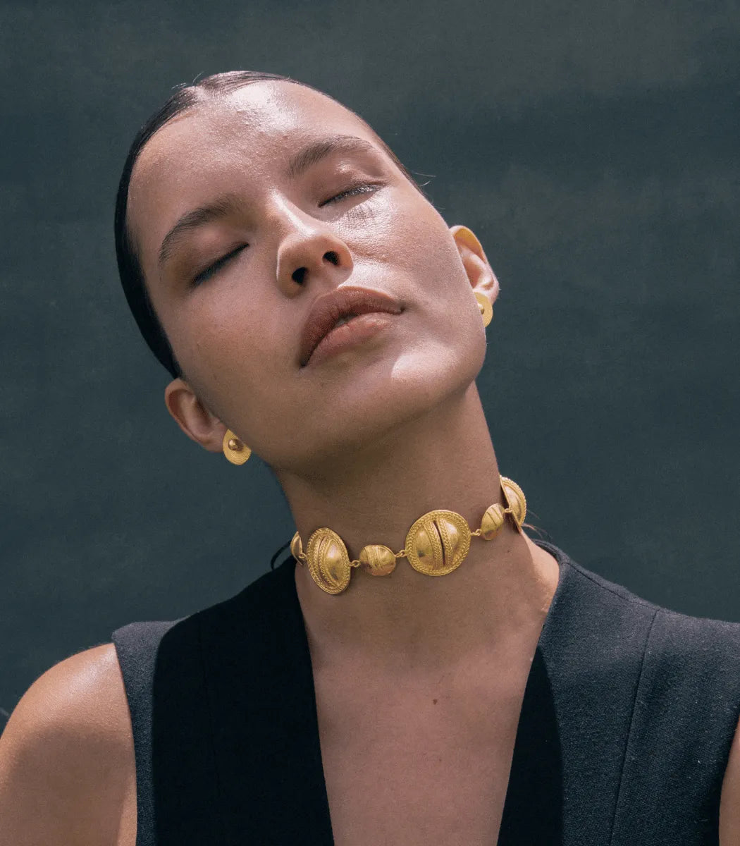 Woman wearing a gold necklace and earrings against a dark background