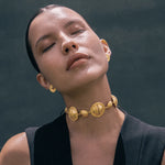 Woman wearing a gold necklace and earrings against a dark background