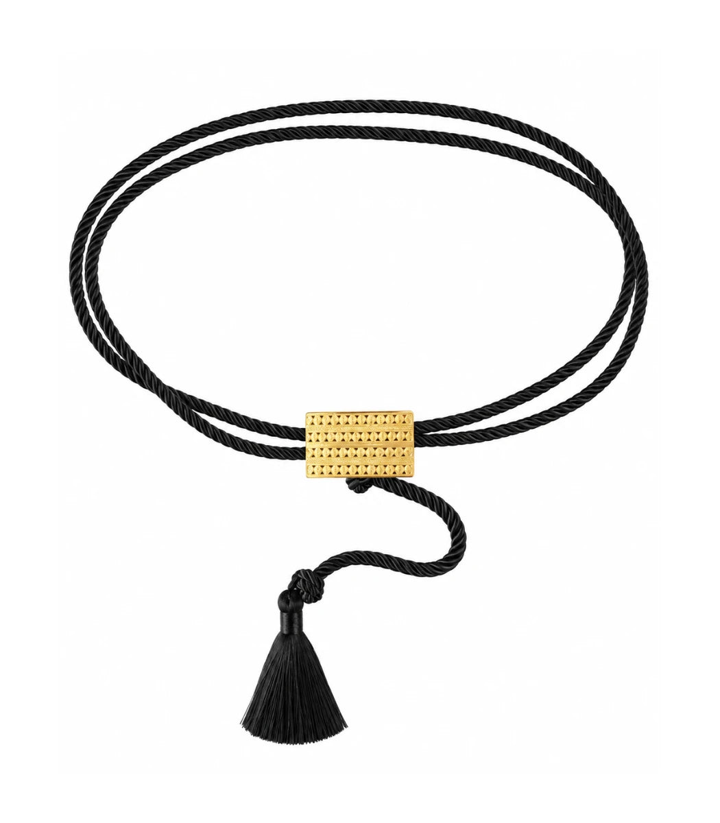 A double-strand black cord bracelet with a textured gold rectangular clasp and a black tassel, shown on a plain white background.
