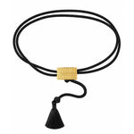 A double-strand black cord bracelet with a textured gold rectangular clasp and a black tassel, shown on a plain white background.