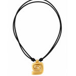 A gold spiral pendant necklace on a black multi-strand cord, shown against a plain white background.